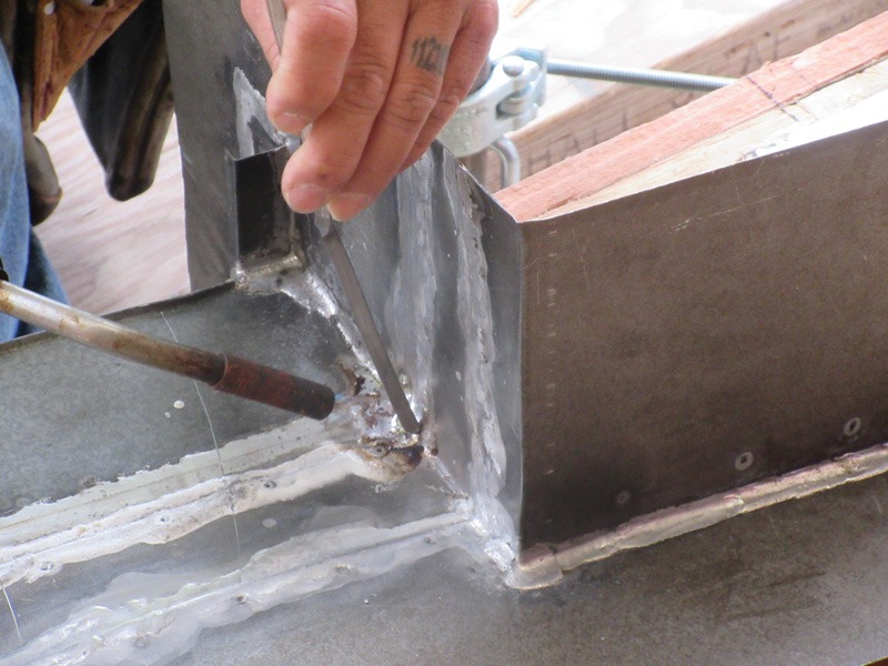Close-up of a person working on a welded metal corner with a clamp and metal rod.