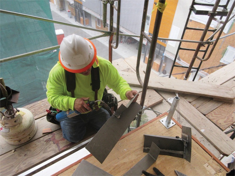 Construction worker in safety gear kneeling on a scaffold and handling metal components.
