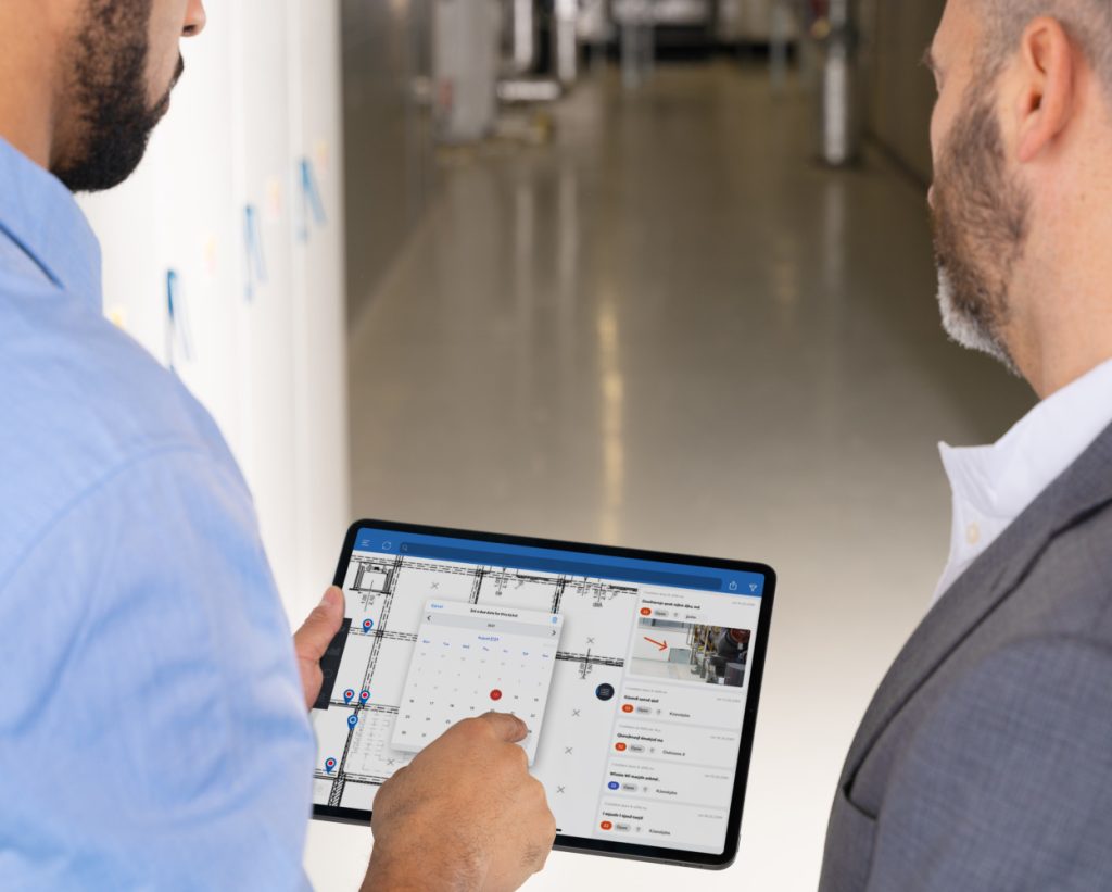 Two men review an architectural floor plan and task list on a tablet.