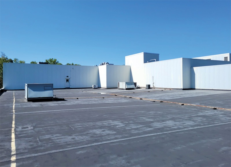 Flat commercial rooftop with white mechanical structures and equipment under a clear blue sky.