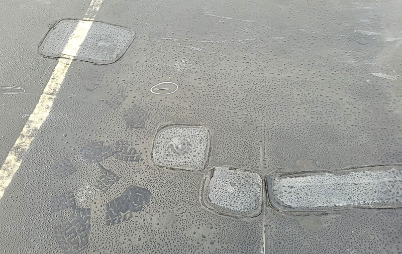 Close-up of rain-speckled asphalt with a faded yellow line and several embedded utility covers.