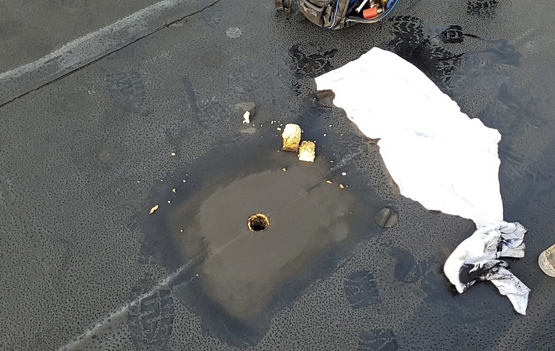 Wet dark surface with a central puddle, scattered yellow fragments, white cloths on the right, and part of a tool pouch at the top.