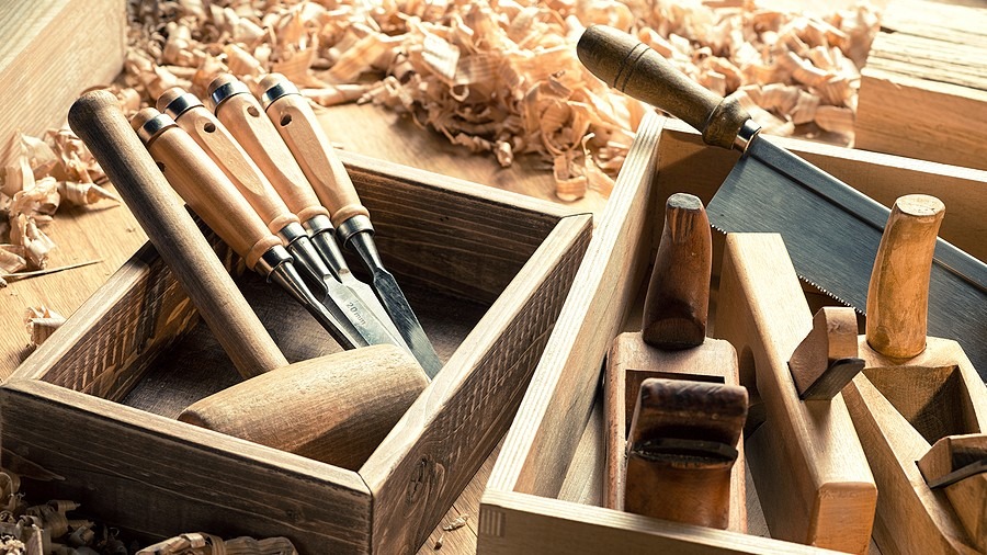 Woodworking chisels, a mallet, and hand planes arranged in wooden boxes amid wood shavings.